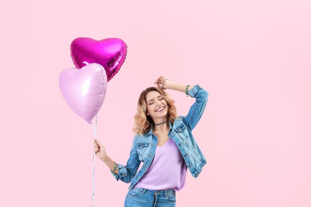 Attraente giovane donna con palloncini d'aria a forma di cuore su sfondo colorato