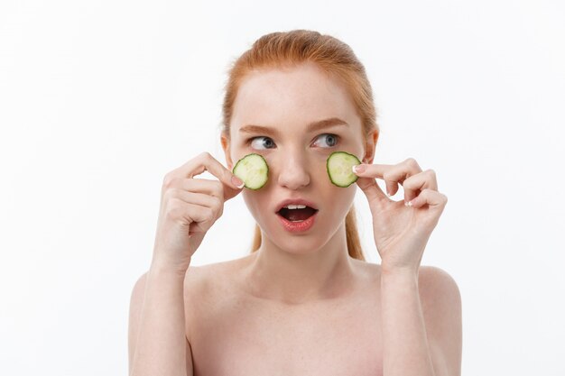 Attraente giovane donna con una bella pelle pulita. Maschera bianca e cetrioli. Trattamenti di bellezza e terapia termale cosmetologica.