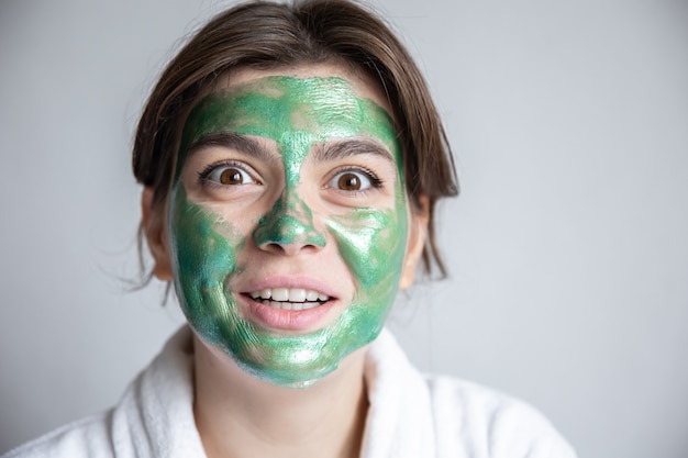 Attraente giovane donna con una maschera cosmetica verde sul viso e in una veste bianca