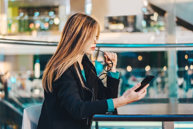 Attraente giovane donna d'affari che passa in rassegna il suo telefono cellulare durante la pausa caffè in un centro commerciale