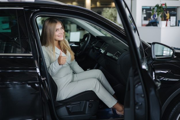 Attraente giovane donna d'affari seduta in macchina nello showroom dell'auto donna che sceglie una nuova auto bella bionda
