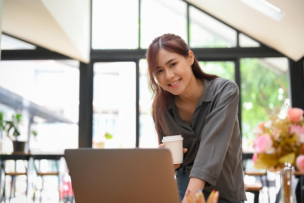 Attraente giovane donna di affari asiatica appoggiata sul tavolo e utilizzando un computer portatile