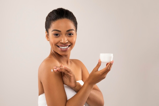 Attraente giovane donna di colore che usa una crema idratante per il corpo dopo la doccia