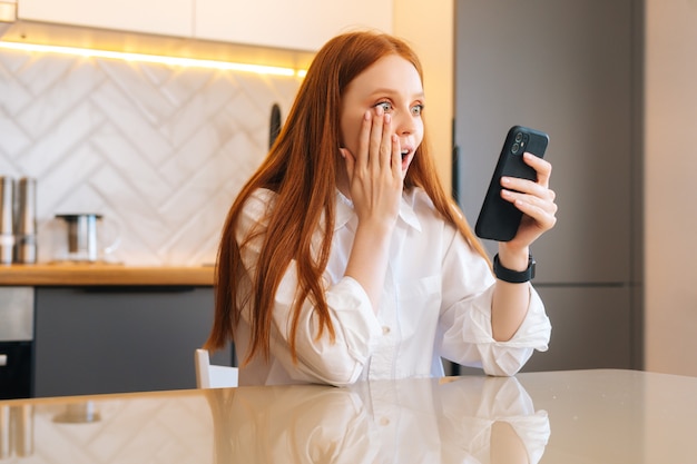 Attraente giovane donna eccitata sorpresa che riceve notizie online sorprendentemente buone sul telefono cellulare