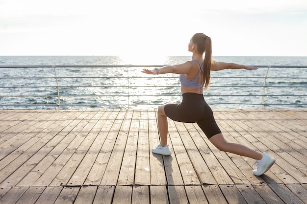 Attraente giovane donna fitness che pratica esercizio di hatha yoga all'alba sulla spiaggia