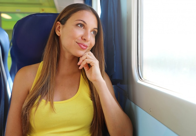 Attraente giovane donna guardando attraverso il finestrino del treno o dell'autobus. Passeggero del treno felice che viaggia seduto su un sedile e guardando attraverso la finestra.