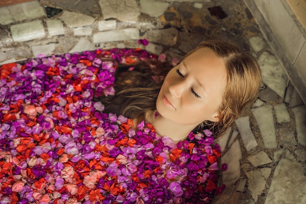 Attraente giovane donna in bagno con petali di fiori tropicali e oli aromatici Trattamenti termali per il ringiovanimento della pelle Donna seducente nel salone Spa Spa di lusso e cura della pelle