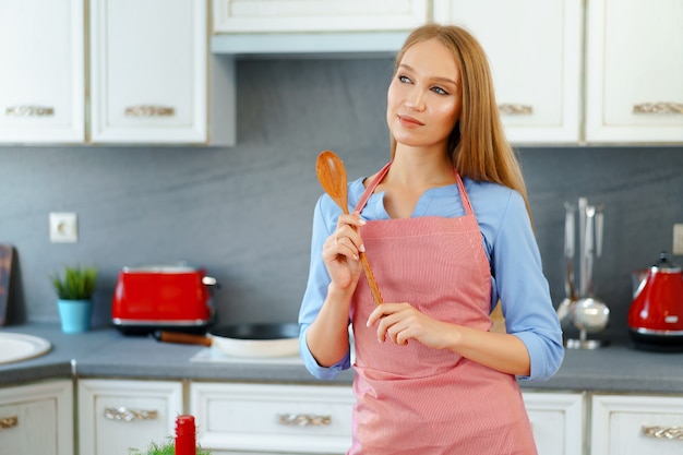 Attraente giovane donna in grembiule rosso in piedi nella sua cucina