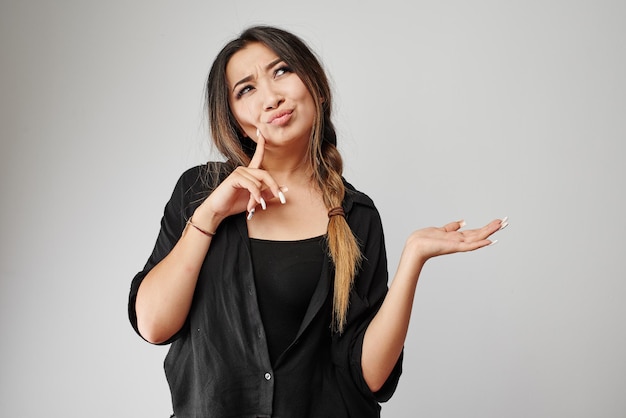 Attraente giovane donna pensosa asiatica kazaka nel pensiero nero totale e finge di tenere il tuo prodotto o testo nel palmo isolato su bianco