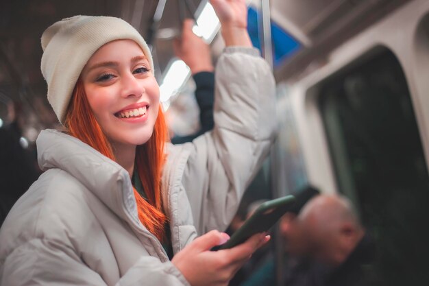 Attraente giovane donna rossa che digita un messaggio e guarda il suo telefono cellulare in un veicolo di trasporto pubblico