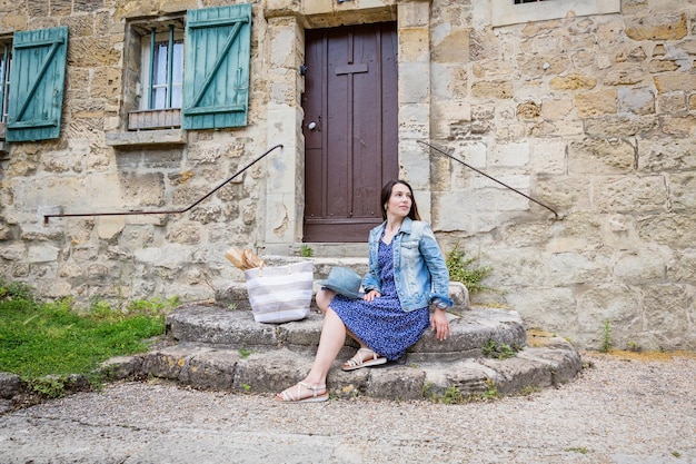 Attraente giovane donna seduta e in posa su antiche scale di pietra all'aperto nella vecchia città francese