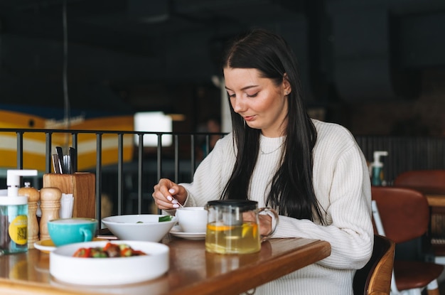 Attraente giovane donna sorridente bruna in casual avendo brunch nel caffè cibo sano