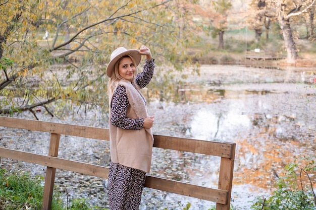 Attraente giovane donna sorridente in abiti alla moda e cappello nel parco autunnale in autunno