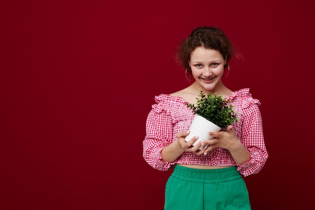 Attraente giovane donna standin e tenendo il fiore in vaso primo piano inalterato