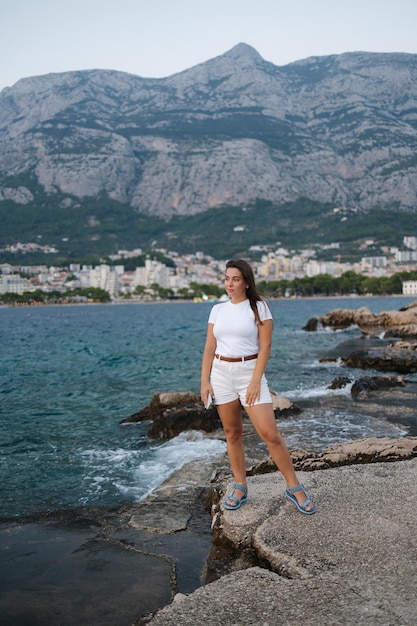 Attraente giovane donna stare sul bordo di una scogliera e guardare il tramonto sul mare Vista posteriore delle montagne