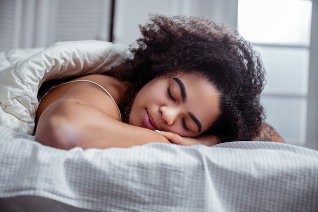 Attraente giovane donna. Tranquilla donna dalla carnagione scura che riposa sul letto e che ha un bel sonno con sogni piacevoli