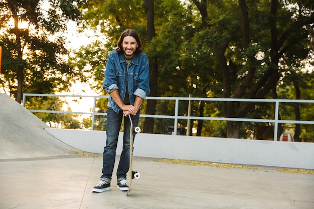 Attraente giovane hipster in piedi allo skate park con uno skateboard