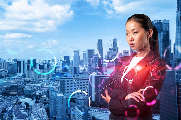 Attraente giovane imprenditrice asiatica che riflette sulla tecnologia al processo aziendale per ottenere un'enorme crescita nel commercio Icone dell'ologramma tecnologico su sfondo di Singapore