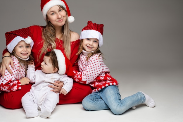 attraente giovane madre in rosso che abbraccia le sue due figlie e il figlio bambino in cappelli di Babbo Natale.