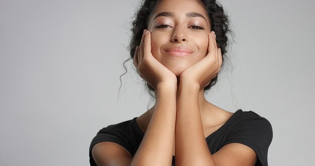 Attraente giovane modella mediorientale che tocca il suo bel viso con una pelle impeccabile e sorridente