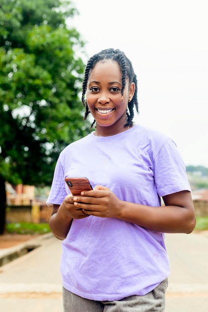 Attraente giovane ragazza nera sorridente tenendo il telefono cellulare e guardando la fotocamera