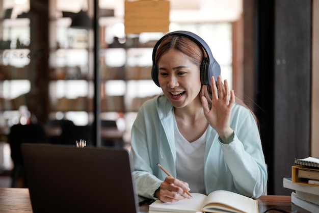 Attraente giovane studente felice che studia online a casa utilizzando le cuffie del computer portatile con chat video sventolando Istruzione a distanza di lavoro a distanza Videoconferenza o evento virtuale in quarantena