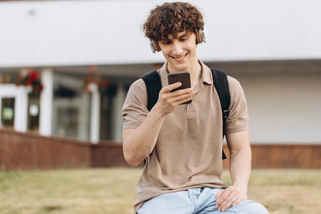 Attraente giovane universitario riccio o studente di college con il telefono che cammina intorno al campus