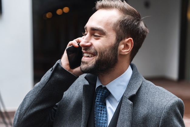 Attraente giovane uomo d'affari che indossa tuta camminare all'aperto, utilizzando il telefono cellulare, parlando