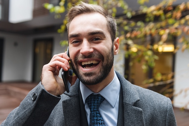 Attraente giovane uomo d'affari che indossa tuta camminare all'aperto, utilizzando il telefono cellulare, parlando