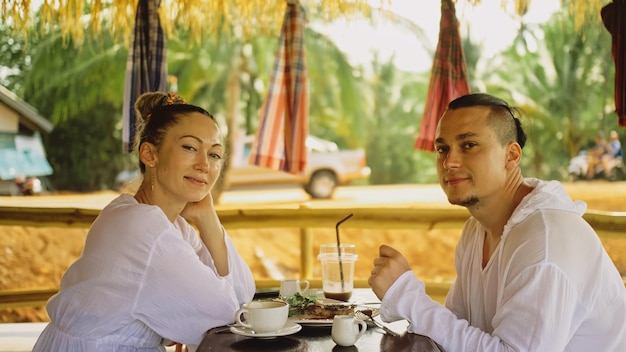 Attraente giovane uomo e donna mangiano e bevono bevande gustose trascorrendo del tempo nel tradizionale caffè galleggiante locale sull'acqua Amorevole coppia felice che fa colazione all'aperto si nutrono a vicenda Vista tropicale