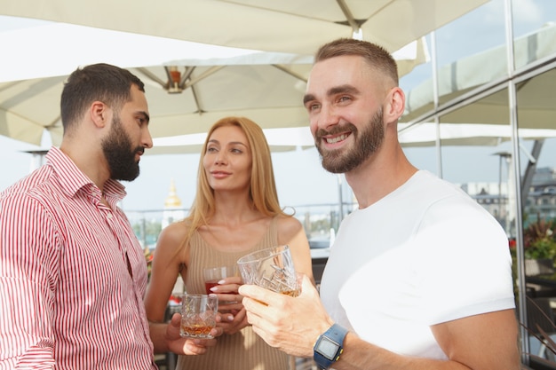 Attraente giovane uomo sorridente, distogliendo lo sguardo con gioia godendo la festa estiva sul tetto al bar