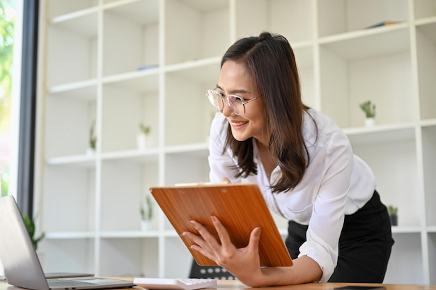 Attraente imprenditrice asiatica appoggiata sul tavolo di lavoro guardando lo schermo del laptop