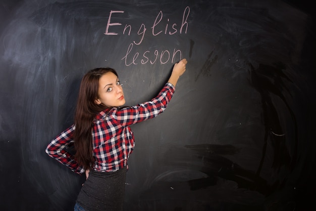 Attraente insegnante di sesso femminile che dà una lezione di inglese scrivendo sulla lavagna della classe e tornando indietro con un'espressione seria verso la telecamera