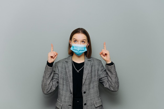 Attraente lavoratrice d'ufficio con una maschera protettiva medica sul viso si erge contro un muro grigio