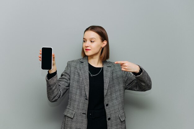 Attraente lavoratrice in giacca tiene uno smartphone con uno schermo nero in mano