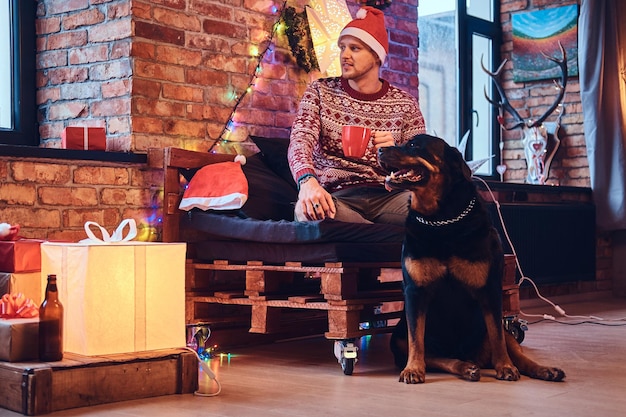 Attraente maschio hipster barbuto con il suo cane Rottweiler in una stanza con decorazioni natalizie.