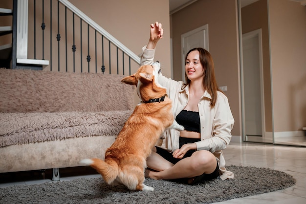 Attraente ragazza abbraccia e gioca con il cane corgi a casa Welsh Corgi Pembroke con la sua proprietaria donna sul pavimento del soggiorno