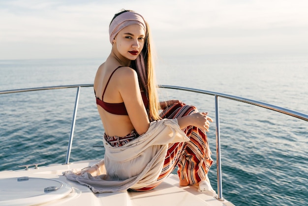 Attraente ragazza alla moda che si gode il tramonto e il mare sul suo yacht in posa