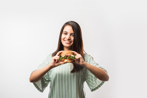 Attraente ragazza asiatica indiana che mangia hamburger su sfondo bianco o giallo