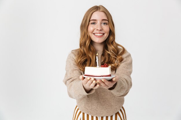 Attraente ragazza che indossa un maglione in piedi isolato su un muro bianco, che mostra la torta di compleanno