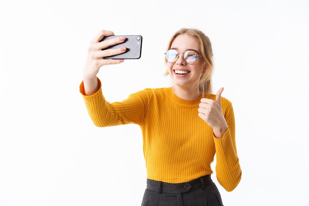 Attraente ragazza che indossa un maglione in piedi isolato sul muro bianco, prendendo un selfie