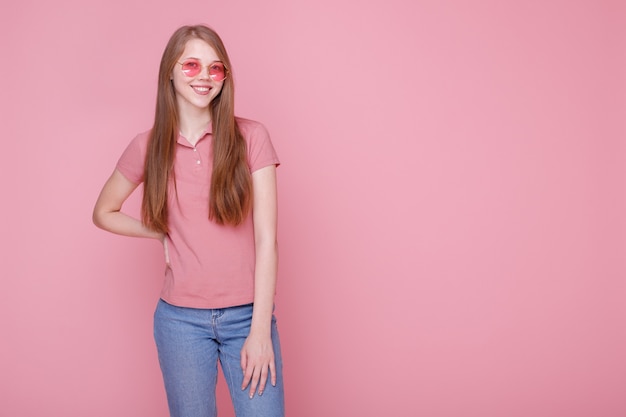Attraente ragazza felice in una maglietta rosa e blue jeans su uno sfondo rosa