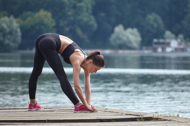 Attraente ragazza in abiti sportivi fa esercizi ginnici su un molo in legno in un parco cittadino.