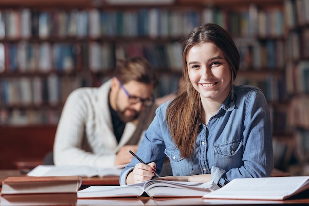 Attraente ragazza seduta alla scrivania e prendere appunti in biblioteca