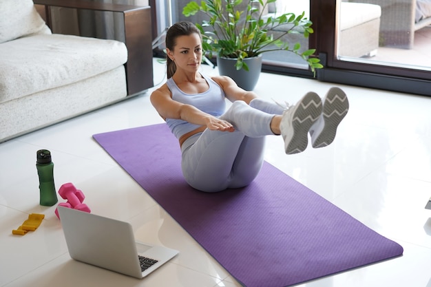 Attraente ragazza snella in abiti sportivi sta facendo esercizi addominali sul pavimento a casa. Uno stile di vita sano.