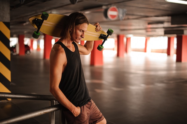 Attraente ragazzo dai capelli lunghi, guardando in basso e in possesso di un longboard