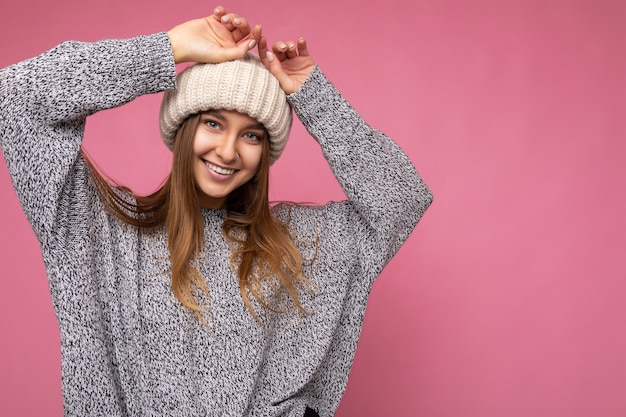 Attraente sorridente felice giovane bionda scura persona di sesso femminile in piedi isolato su sfondo colorato parete indossando tutti i giorni vestito elegante che mostra le emozioni del viso guardando la fotocamera