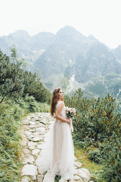 Attraente sposa bruna in splendido abito da sposa bianco in piedi vicino al lago Morskie Oko