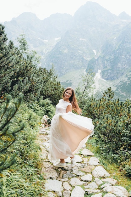 Attraente sposa bruna in splendido abito da sposa bianco in piedi vicino al lago Morskie Oko