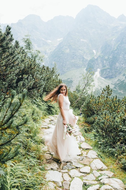 Attraente sposa bruna in splendido abito da sposa bianco in piedi vicino al lago Morskie Oko